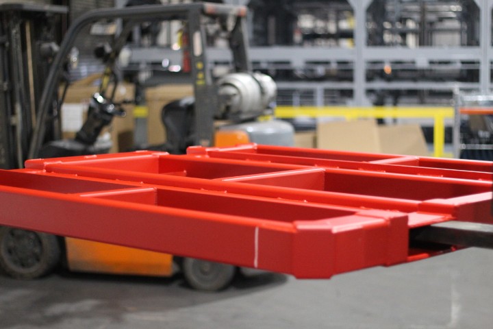 Forklift lifting a red metal pallet with a second forklift operating in the background
