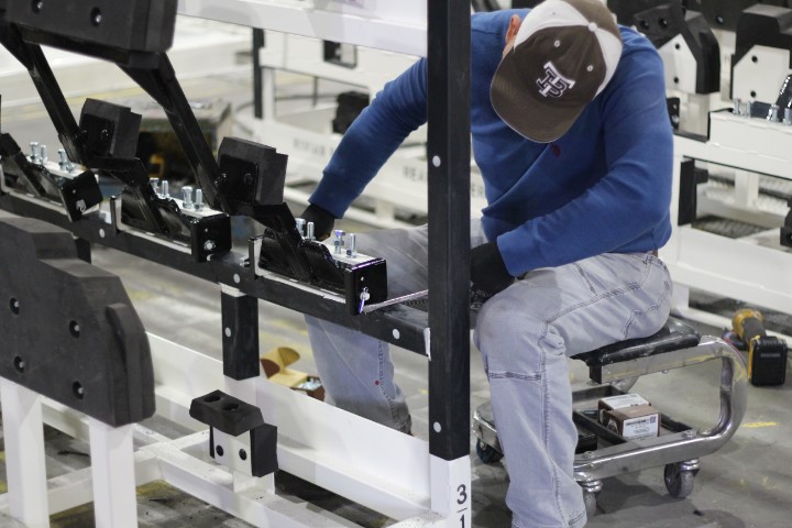 Worker in a blue shirt and hat assembling components on a white steel rack
