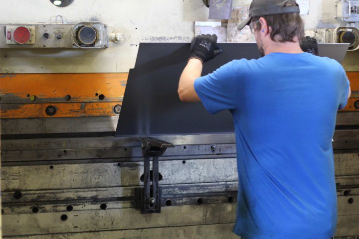 Worker in a blue shirt holding a sheet of metal at a press brake