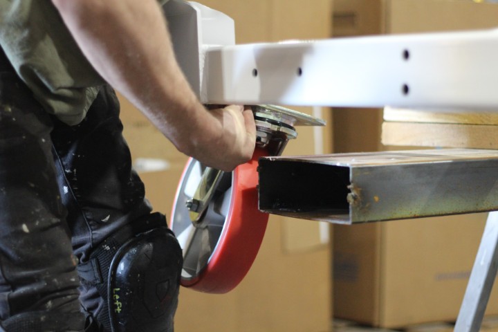 Worker installing a red caster on a white steel cart