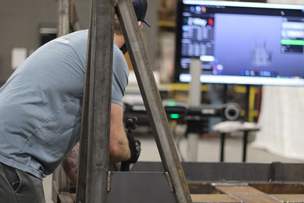 Worker scanning a steel rack with measurement equipment and a monitor in the background