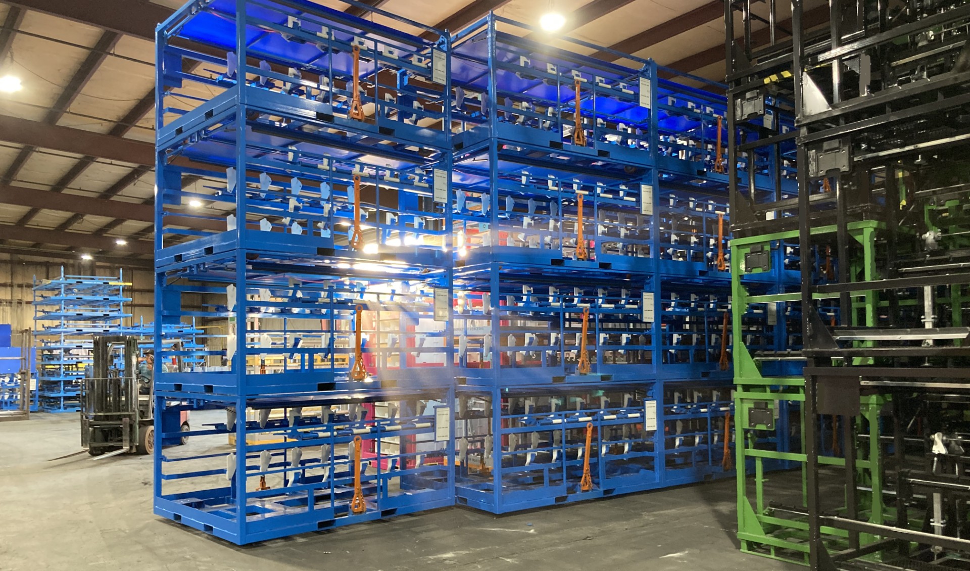 Stacked blue shipping racks in a warehouse with green and black racks nearby