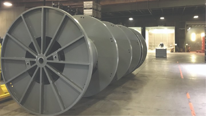 Row of large gray steel cable reels lined up on the shop floor