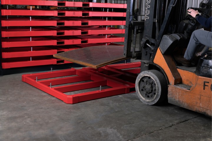 Forklift loading sheet metal stock onto a custom red sheet metal storage rack on the shop floor.