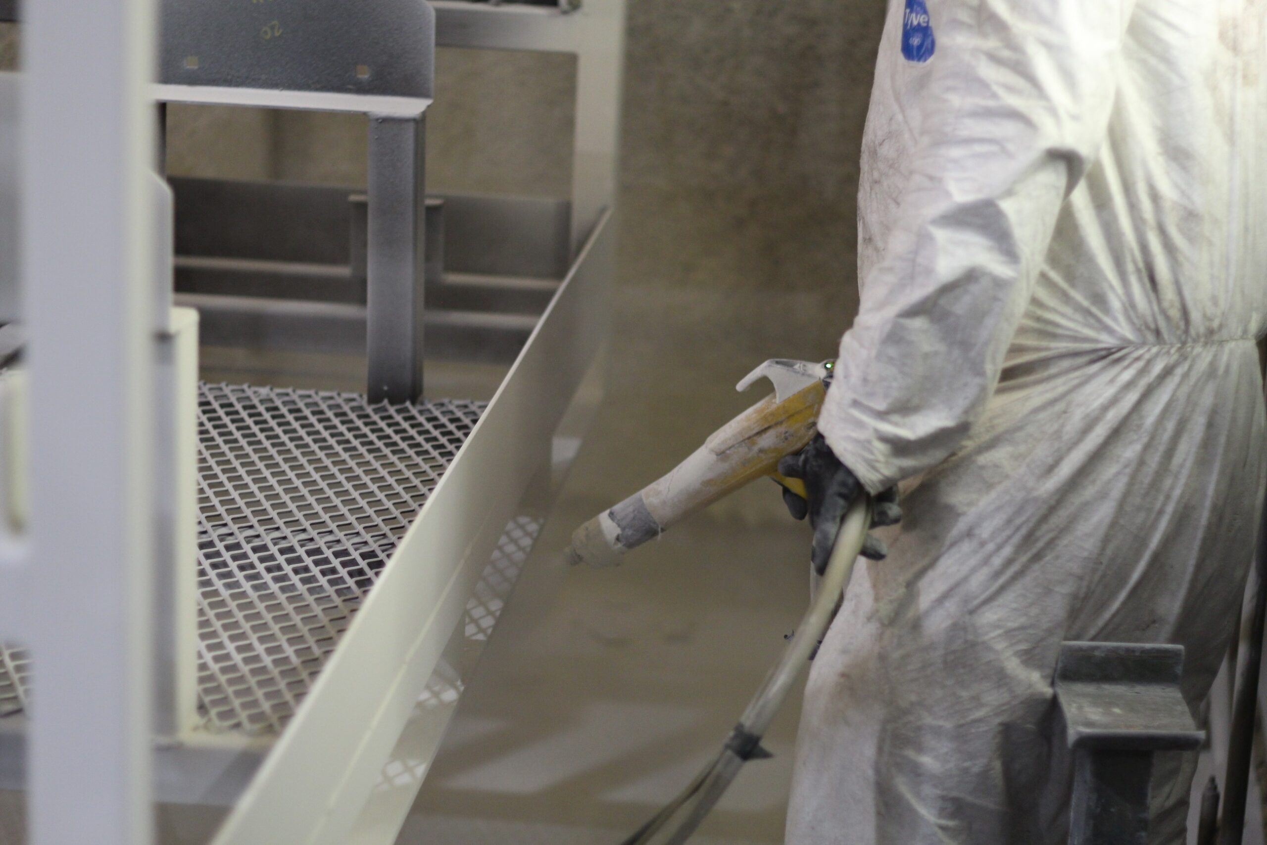 Technician applying a white powder coat finish to custom metal parts in the in-house finishing department.